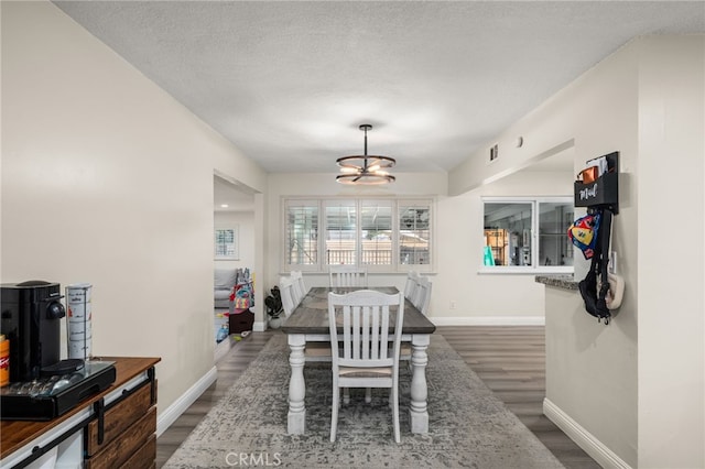 dining space with dark wood-style flooring, a textured ceiling, and baseboards