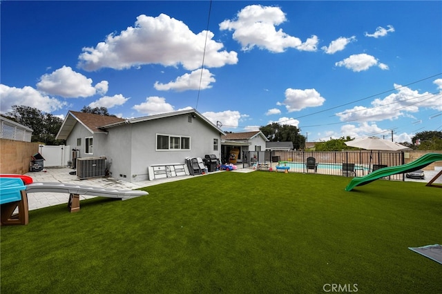 back of property with a lawn, fence, cooling unit, a playground, and stucco siding