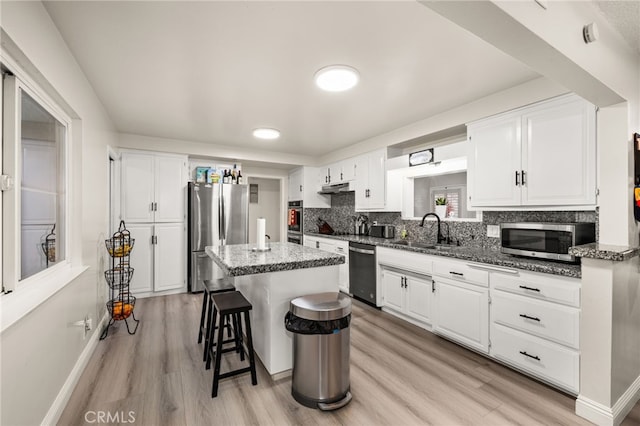 kitchen with stainless steel appliances, a kitchen island, a sink, white cabinets, and dark stone counters