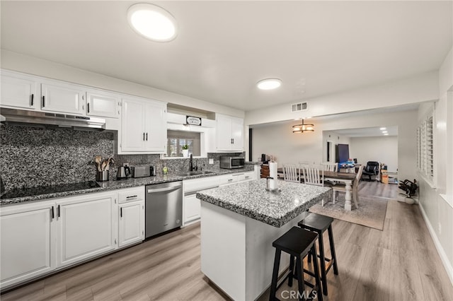 kitchen with a kitchen island, black electric cooktop, stainless steel dishwasher, under cabinet range hood, and a sink