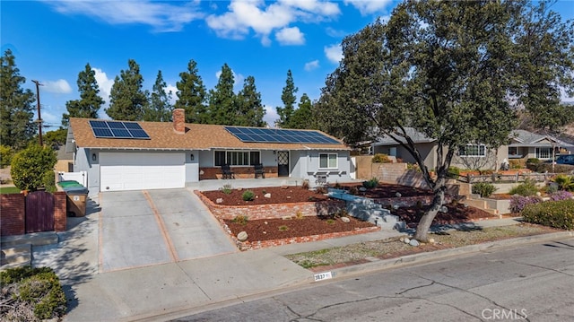 single story home featuring a chimney, solar panels, an attached garage, fence, and driveway