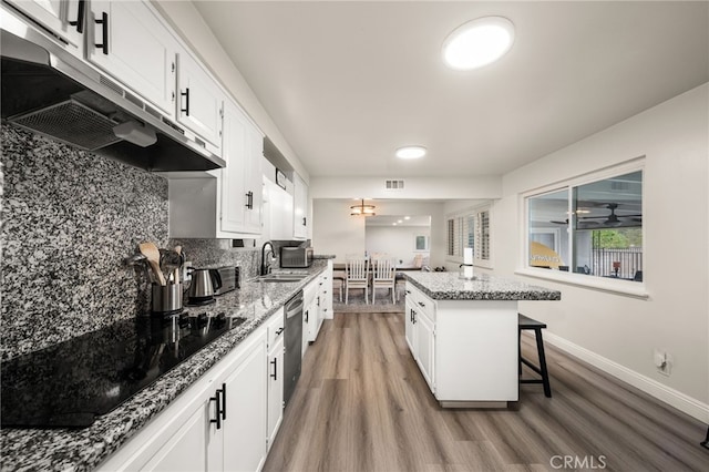 kitchen featuring a breakfast bar area, a center island, black electric stovetop, under cabinet range hood, and white cabinetry