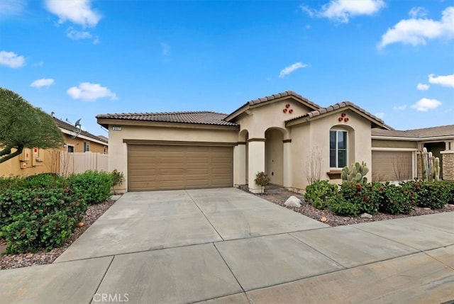 mediterranean / spanish home featuring a garage, fence, driveway, a tiled roof, and stucco siding