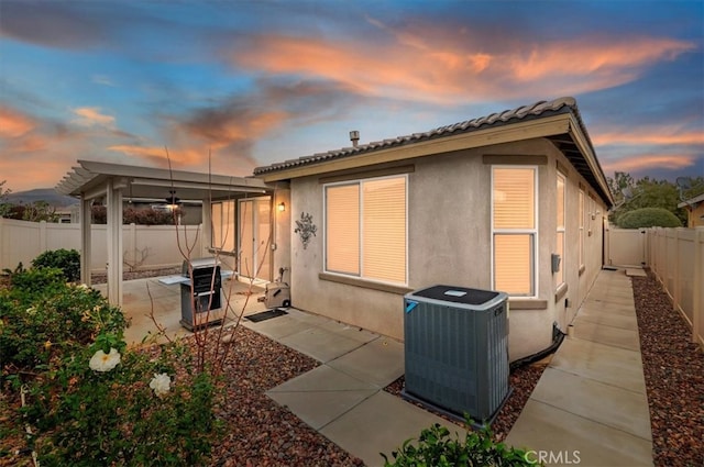 back of property at dusk featuring a patio, stucco siding, central air condition unit, ceiling fan, and a fenced backyard