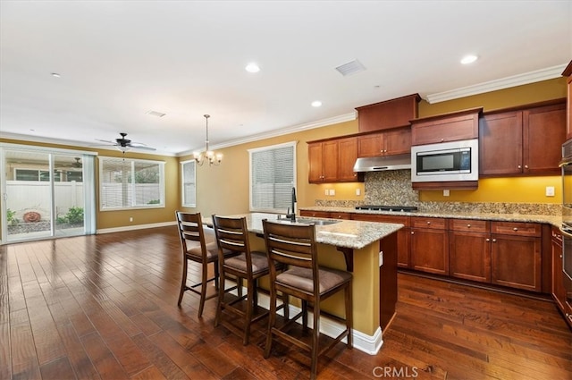 kitchen featuring gas stovetop, visible vents, stainless steel microwave, a sink, and under cabinet range hood