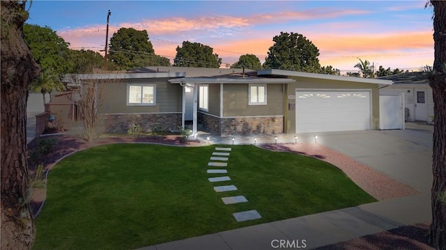 view of front of home featuring driveway, a garage, stone siding, a yard, and stucco siding