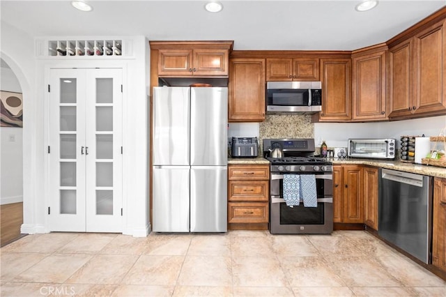 kitchen with appliances with stainless steel finishes, brown cabinets, a toaster, and light stone countertops