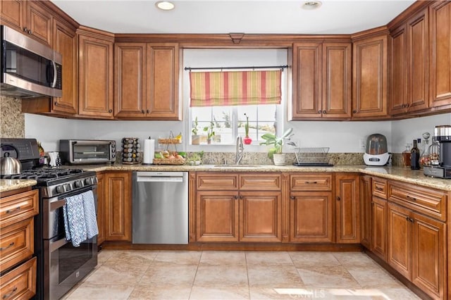 kitchen featuring brown cabinets, a toaster, light stone counters, and stainless steel appliances