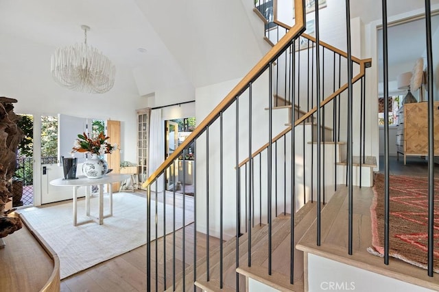 stairs featuring high vaulted ceiling, a chandelier, and wood finished floors
