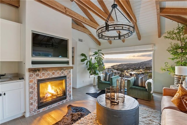living room featuring lofted ceiling with beams, visible vents, a brick fireplace, baseboards, and wood finished floors