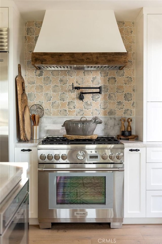 kitchen featuring backsplash, white cabinets, custom exhaust hood, and stainless steel stove