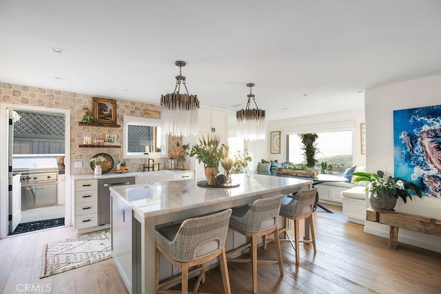 kitchen with a center island, a breakfast bar, hanging light fixtures, light wood finished floors, and white cabinets