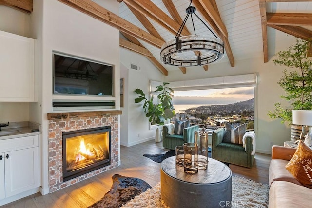 living room with lofted ceiling with beams, wood finished floors, a brick fireplace, baseboards, and visible vents