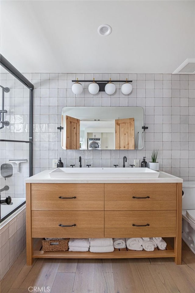 bathroom with tile walls, toilet, double vanity, tiled shower / bath, and wood finished floors
