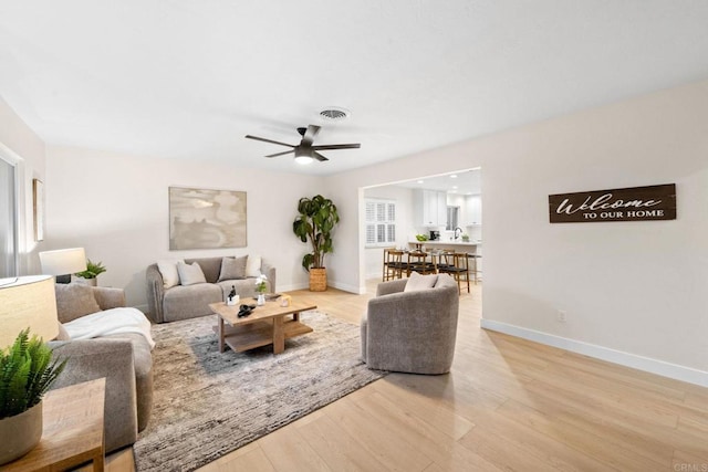 living area with light wood finished floors, baseboards, visible vents, and a ceiling fan