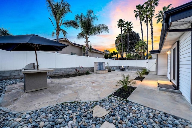 patio terrace at dusk with a fenced backyard and an outdoor kitchen