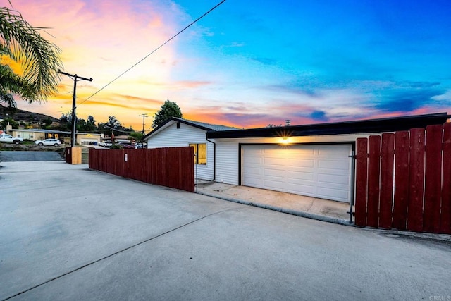 garage at dusk with a detached garage and fence