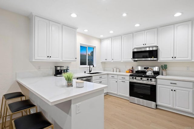 kitchen featuring stainless steel appliances, a peninsula, a sink, white cabinetry, and light countertops