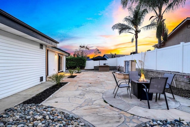 patio terrace at dusk with an outdoor fire pit and a fenced backyard