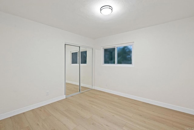 unfurnished bedroom featuring light wood-type flooring, baseboards, and a closet