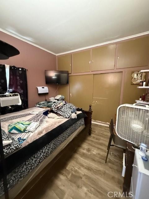 bedroom with ornamental molding, a decorative wall, and wood finished floors