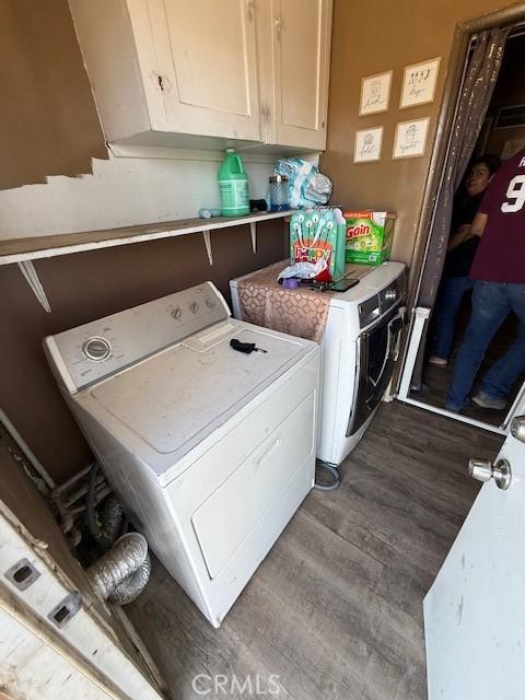 clothes washing area featuring dark wood-style flooring, washing machine and clothes dryer, and cabinet space