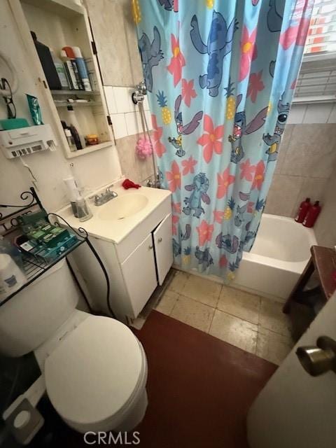 full bath with toilet, tile patterned floors, shower / bath combo with shower curtain, vanity, and tile walls