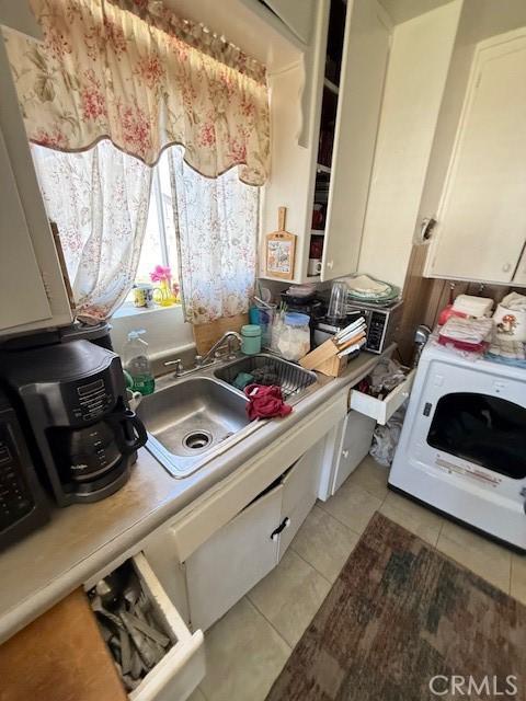 kitchen featuring light tile patterned floors, white cabinetry, washer / clothes dryer, and a sink