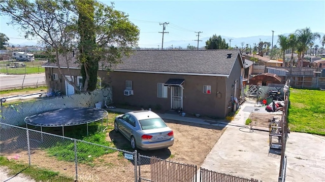 view of front of house with a shingled roof, a trampoline, fence private yard, and stucco siding