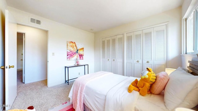 bedroom with light carpet, visible vents, and multiple closets