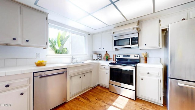 kitchen with stainless steel appliances, tile counters, a sink, and white cabinetry