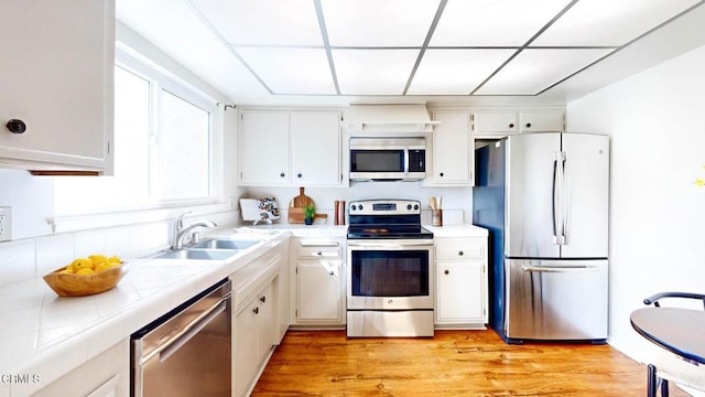 kitchen with tile countertops, stainless steel appliances, a sink, and white cabinets