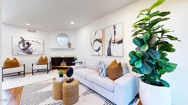 living area with a fireplace with raised hearth, recessed lighting, wood finished floors, visible vents, and baseboards