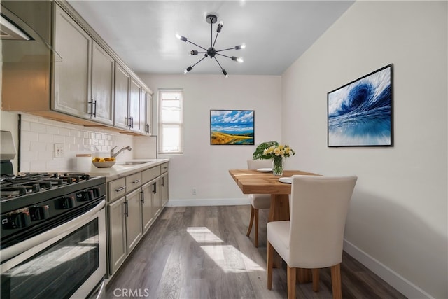 kitchen featuring stainless steel gas range oven, decorative backsplash, dark wood-style flooring, gray cabinets, and a sink