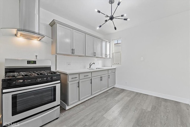 kitchen with light wood-style flooring, light countertops, wall chimney range hood, tasteful backsplash, and stainless steel range with gas stovetop