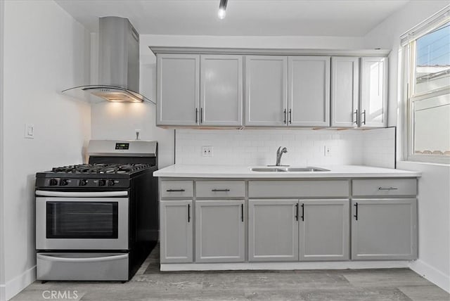 kitchen with a sink, light wood-style floors, wall chimney range hood, backsplash, and stainless steel gas stove