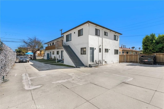 rear view of house featuring entry steps, fence, and stucco siding