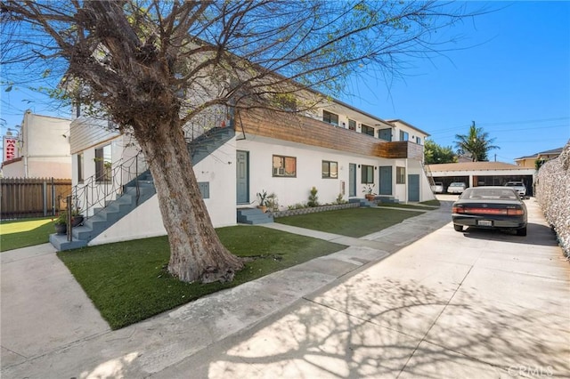 view of front of home featuring stucco siding, fence, concrete driveway, and a front yard