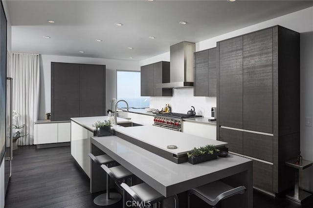 kitchen with a sink, stainless steel stove, light countertops, wall chimney exhaust hood, and modern cabinets