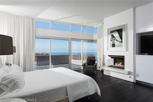 bedroom with access to outside, dark wood-style flooring, and a warm lit fireplace