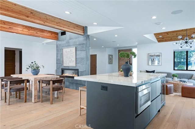 kitchen with a spacious island, open floor plan, decorative light fixtures, light wood-style floors, and beam ceiling