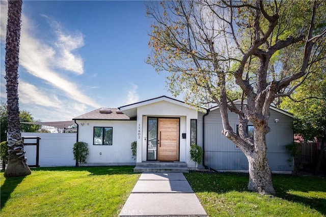 view of front of house featuring fence, a front lawn, and stucco siding