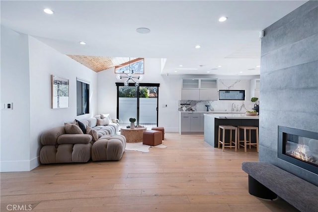 living room with light wood-type flooring, lofted ceiling, a tiled fireplace, and recessed lighting