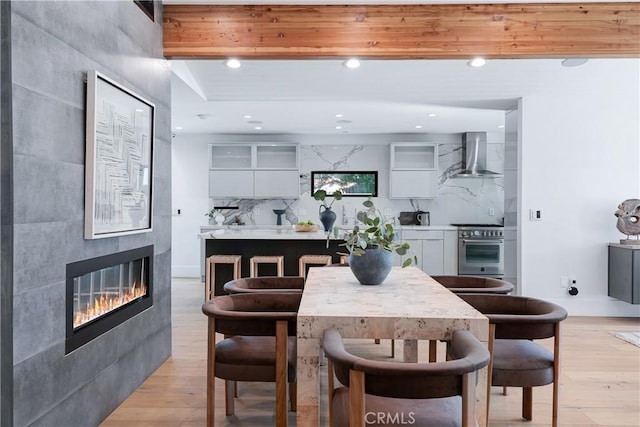 dining area featuring light wood-style floors, recessed lighting, beamed ceiling, and a tiled fireplace