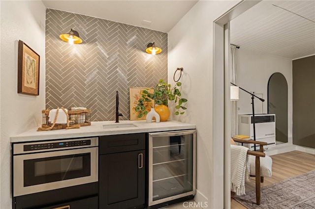 bar featuring tile walls, an accent wall, a sink, light wood-type flooring, and beverage cooler