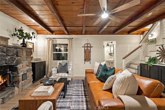 living room featuring beam ceiling, a fireplace, wood ceiling, and a ceiling fan