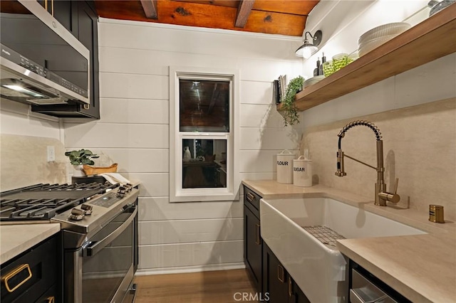 kitchen with appliances with stainless steel finishes, light countertops, dark cabinetry, open shelves, and a sink