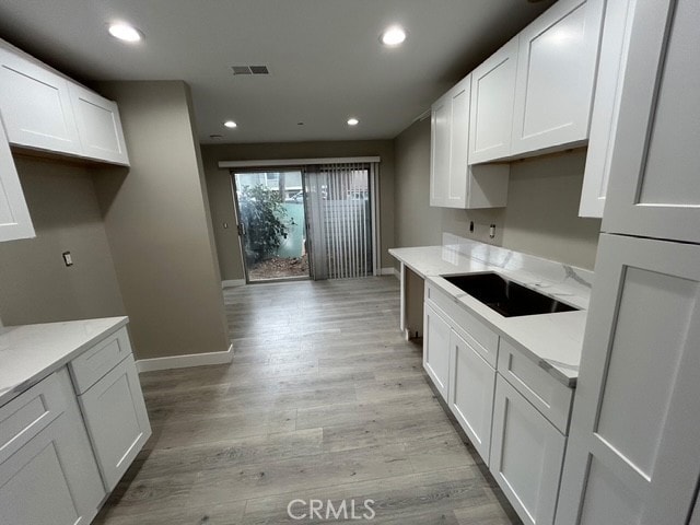 kitchen featuring recessed lighting, white cabinets, light wood-style flooring, and baseboards