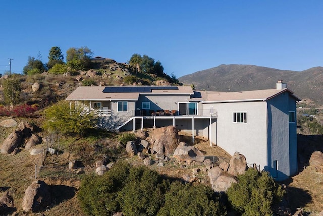 back of property featuring a deck with mountain view, stairs, solar panels, and stucco siding