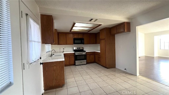 kitchen featuring black microwave, stainless steel stove, a sink, light countertops, and brown cabinets